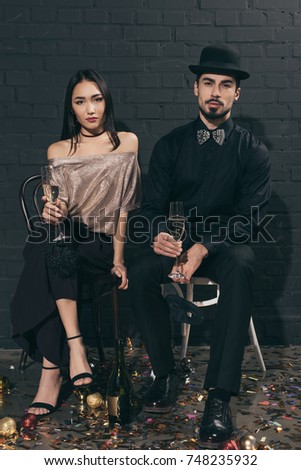 fashionable multicultural couple with glasses of champagne looking at camera at new year party