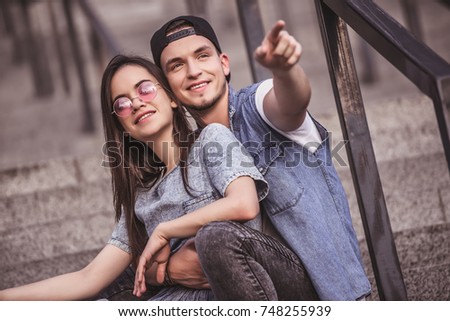 Stylish young couple is hugging, talking and smiling while sitting on stairs in city