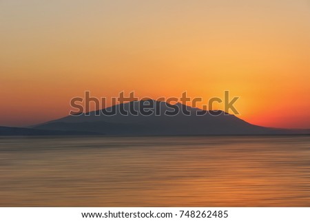 Burning Nea Vrasna sunrise in Greece. The Sun is rising behind the mountains and throwing first light  at sea.