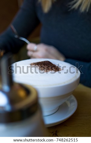 Big cup of coffee with blurry girl in the background