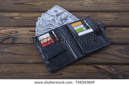 Black natural leather wallet, on a wood table background. Expensive men's wallet close-up. A purse filled with money and plastic cards. Idea: business, banking