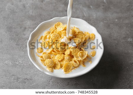 Pouring milk into plate with cornflakes on table