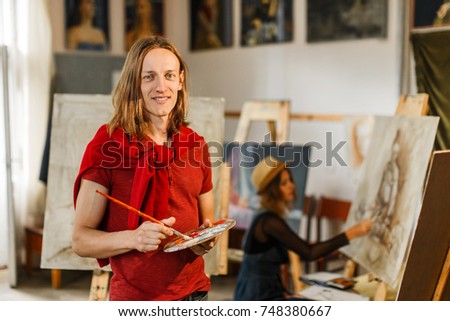 Long hair caucasian male artist smiles near the picture in the studio
