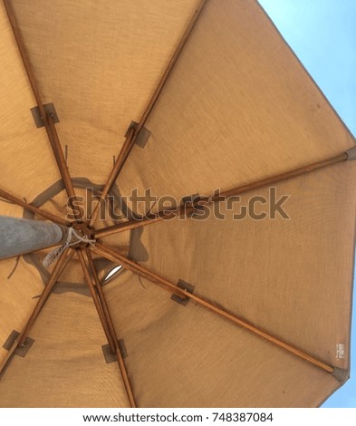 bottom floor perspective view photography looking up at the sun umbrella parasol with a geometric pattern fabric color orange beige with a blue sky as background 