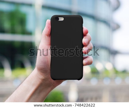 Smart phone on a blurry city background in a black plastic case back view. Smart phone in man's hand. Template of phone case Royalty-Free Stock Photo #748422622