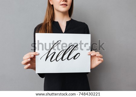 Close up photo of young woman standing and holding postcard on gray background