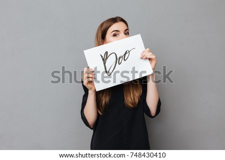 Portrait of pretty girl standing and covering her face while holding postcard on gray background