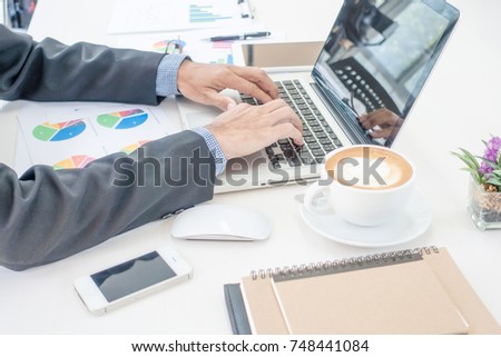 A man woring at business office desk with laptop, paper analysis and coffee.