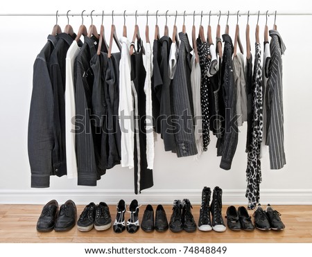 Female and male black and white clothes on a rod and shoes on a wooden floor. Royalty-Free Stock Photo #74848849