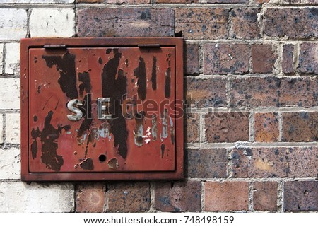 An abrasive red security box on a two tone red-brown and white brick wall