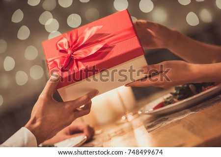 Cropped image of young couple holding a gift box while celebrating New Year in a restaurant