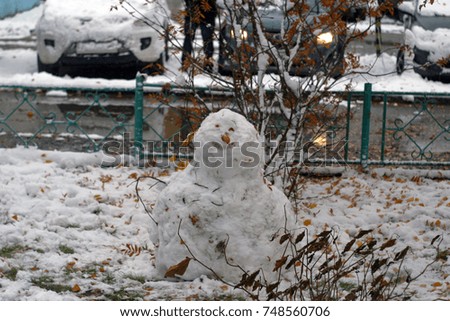 A snowman made of white snow, decorated with eyes and a nose-carrot in the town yard. The first snow in autumn, in October. Autumn and winter background