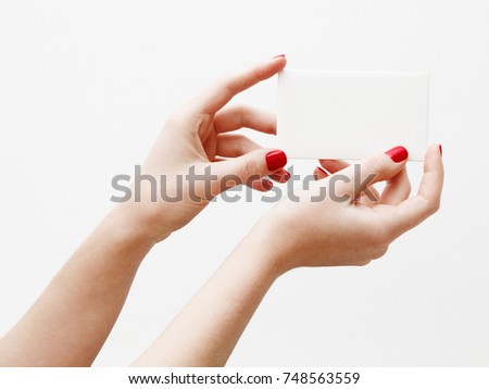 Flat lay, top view. Beauty and fashion concept. Beautiful female hands with red manicure. Minimal style. Minimalist photography. Pale composition with girl's hand holding card on white background