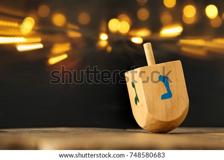 Image of jewish holiday Hanukkah with wooden dreidel (spinning top) and gold lights on the table