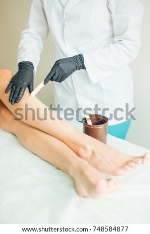 close up Beautician waxing female legs in spa center