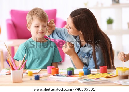 Cute boy with mother painting at table indoors