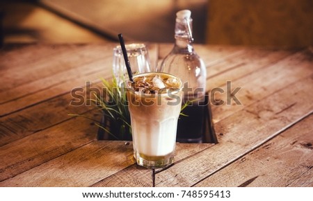 Ice coffee latte in a transparent mug on the wooden table with artificial green plant and glass bottle.Selective focus shot with retro filter effects.