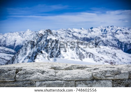 A stone tabletop with space for your product or advertising text. View of winter alpine mountains. Beautiful December sky in blue color.