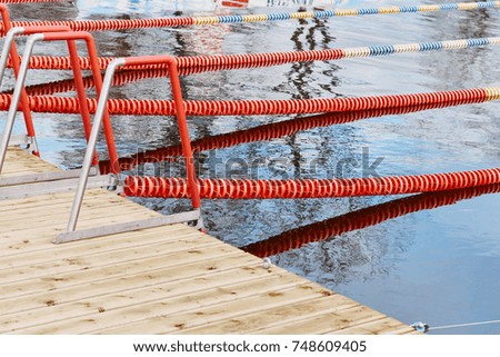 Outdoor sports swimming pool With Blue, White and Red Lap Lines, wooden footbridge, metal stairs in water, without people