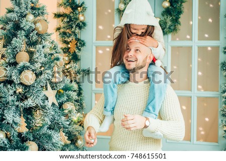 Young girl helping her father decorating the Christmas tree, holding some Christmas baubles in her hand