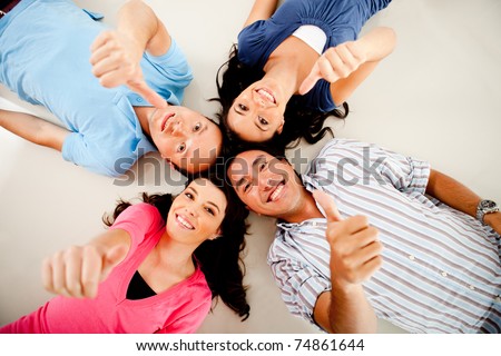 Group of friends with their heads together on the floor and thumbs up - isolated