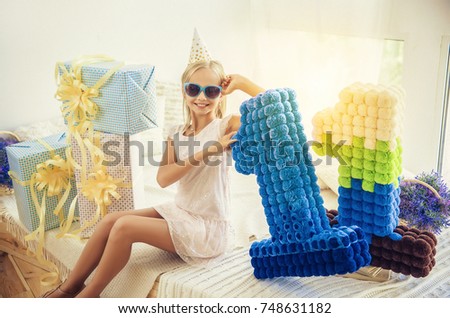 Cute, smiling birthday girl posing in the pile of gift boxes with celebration hat and sunglasses