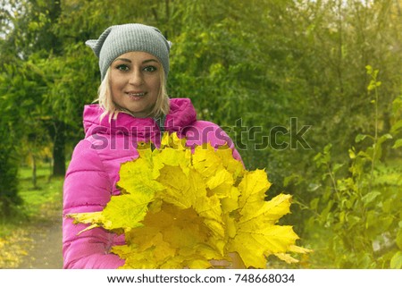 beautiful blonde girl in pink jacket with bouquet of leaves