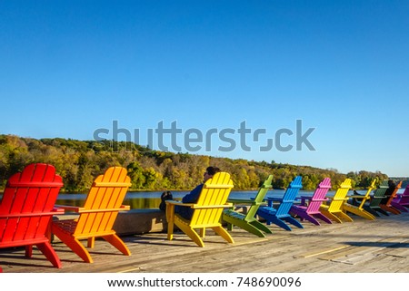 Man relaxing in a row of brightly colored adirondack chairs along waterfront in fall