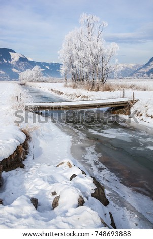 The bridge through the frozen rivulet against the background of the winter Alpine landscape, Austria