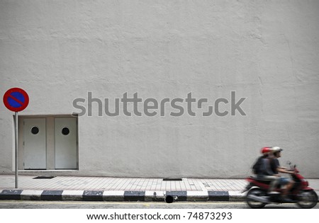 An empty concrete wall with copyspace for text along a street with a motorbike driving by. Royalty-Free Stock Photo #74873293