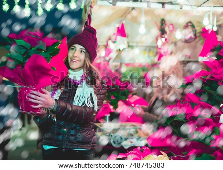 Young smiling teenager girl staying near counter with poinsettia at Xmas market