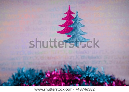 Christmas photography picture with tree shape decorations hanging up in pink and blue with glitter and matching color tinsel and white shiny Merry Christmas text wrapping paper background