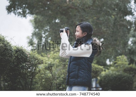 Beautiful Asian girl  in warm clothes with retro  camera shooting a photo in the park