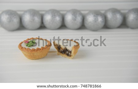 Christmas food photography image with silver color tree decoration glitter baubles in background and spice iced mince pies on white wood taken in studio on South coast of England UK