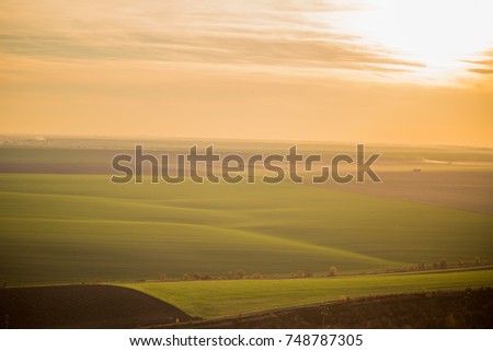 an aerial photograph of an unlimited green field at sunset, where different stripes of the field merge with the horizon of the evening sky