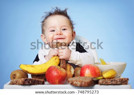 Cute Baby boy eating healthy food for breakfast on bright blue background: horizontal