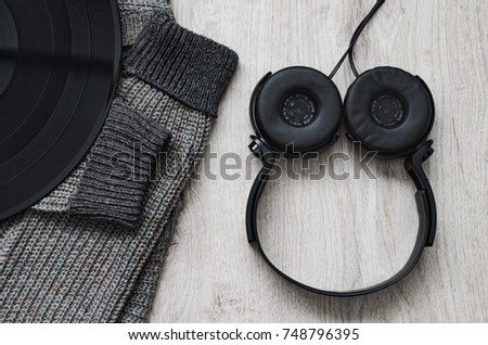 Composition, woolen sweatshirt black headphones and a large vinyl record on a wooden background.