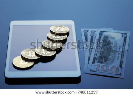Tablet computer, bitcoins and hundred dollar bills on a dark background. The concept of virtual business and currency.