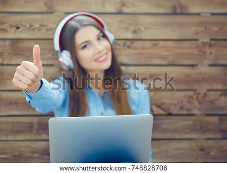 Young happy smiling brunette woman with headphones sitting with outstretched hand and thumb up. Girl listening music in headphones. Photo with depth of field.