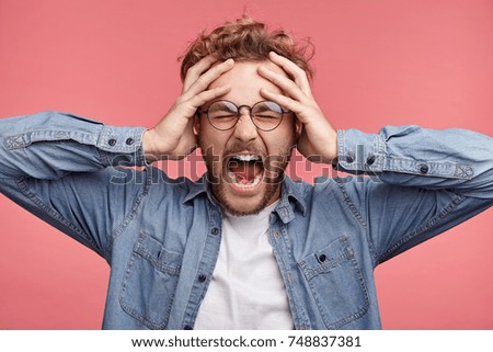 Stressful hipster male scremas in panic, closes eyes in terror, keeps hands on head, finds out terrified news or disaster about best friend, can`t believe of his death. People, stress, annoyance Royalty-Free Stock Photo #748837381