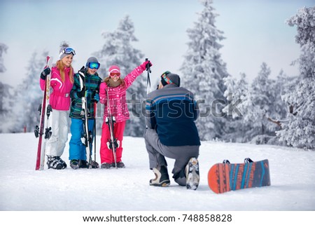 father taking picture of happy family standing in snow on the mountain