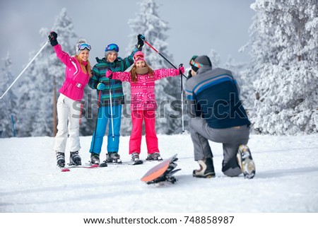 father taking picture of happy family on ski holiday in mountains