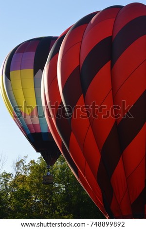 Two hot air balloons rising from the floor bottom ground into the sky background blue with a tree bushy forest green leaves colorful red and black geometric pattern
