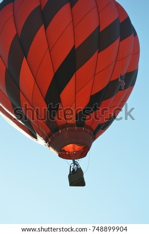 Vertical photography portrait picture view of a hot air balloon rising up into the light blue sky colored black and red vintage transportation geometric diamond pattern