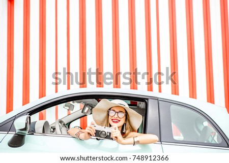 Woman in the car on the red wall background during the summer vacation. Wide angle view with copy space