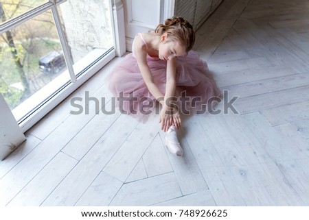 Closeup of young ballerina sit in pointe shoes at white wooden floor background, with copy space. Ballet practice. Beautiful slim graceful ballet dancer.