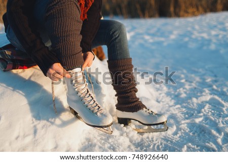 Woman lacing ice skates at the edge of a frozen lake. Cropped image of a woman putting ice skates on.