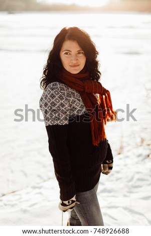Woman in knitted jumper and scarf  against snowy background. Thoughtful woman standing at the edge of an empty frozen lake.