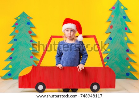 Child with Christmas hat driving a car made of cardboard. Christmas concept. New Year's holidays.