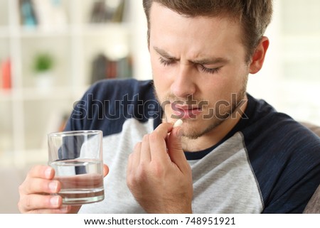 Man suffering taking a pill sitting on a sofa in the living room in a house interior Royalty-Free Stock Photo #748951921